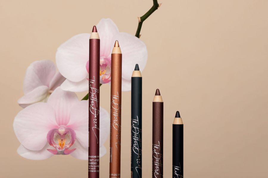 A line of makeup pencils in front of a flower.